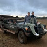 Zwei Vögele-Mitarbeiterinnen sitzen bei bewölktem Himmel auf dem Safari-Fahrzeug in der Steppe des Amakhala Game Reserves in Südafrika.